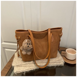 Close-up of brown suede tote bag featuring a cute plush bear charm and side drawstring
