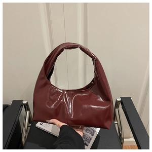 Detail of burgundy patent leather crescent bag featuring vertical stitching and glossy finish