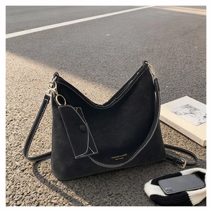 Detail of black suede tote bag with white contrast stitching and gold metal hardware