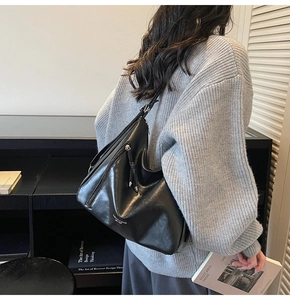Rear view of a minimalist black leather hobo tote bag worn with a casual knit sweater