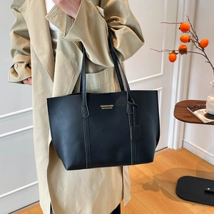 Detail view of smooth black leather tote bag with gold logo and stylish shoulder straps