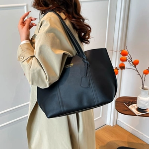Close-up of black matte tote bag with thin straps on beige trench coat model