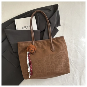 Close-up of brown leopard pattern tote bag with teddy bear charm and stripe tassel