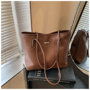 Detail of a brown lychee pattern leather tote bag placed on a book in a sunlit room