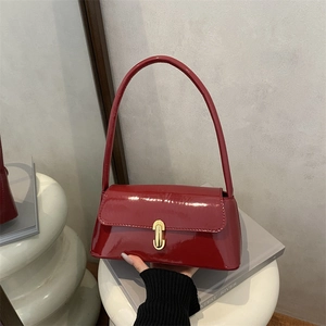 Glossy burgundy patent leather handbag with gold U-shaped buckle on an art base