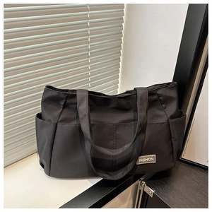 Detail view of the side pocket and grey 'FASHION' label on this black nylon tote bag