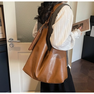 Detail of a large brown hobo tote bag featuring side metal zipper and grainy leather texture