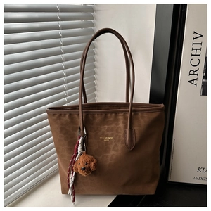 Detail of leopard print tote bag featuring a plush bear charm and brand logo on dark brown