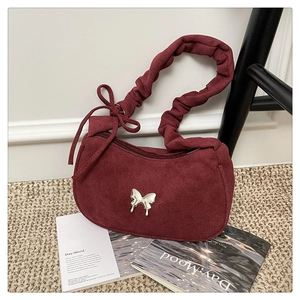 Close-up of a burgundy suede underarm bag with a silver butterfly metal buckle detail