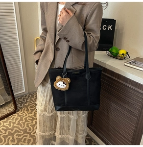 Detail of minimalist black tote bag with plush bear charm and fashion label tag