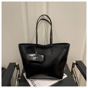 Detail of a large black glossy tote bag on a leather chair showing smooth mirror finish