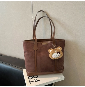 Detail of dark brown suede tote bag featuring fashion tag and plush cartoon charm