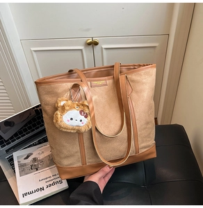 Detail of earthy tote bag with suede texture, brown leather trim and plush pendant