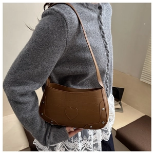Detailed close-up of brown crocodile pattern shoulder bag with silver rivets and heart patch