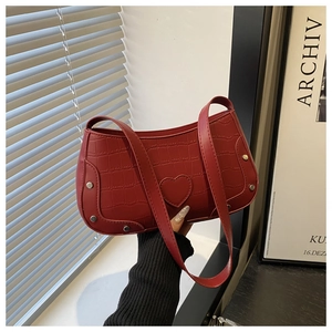 Detail of red croc-embossed underarm bag featuring a heart patch and silver rivets