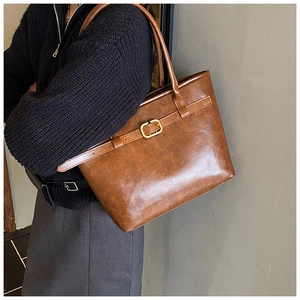 Close-up of brown vintage leather tote bag with gold buckle detail on a female model