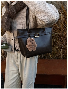 Detail of dark brown leather tote bag with gold buckle and teddy bear charm in autumn setting