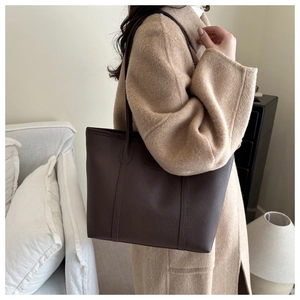 Detail of dark brown pebble leather tote bag shown on model with camel coat