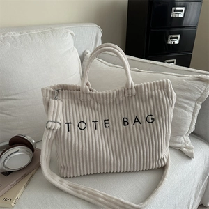 Minimalist beige corduroy tote bag with black embroidery on a white fabric sofa