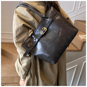 Close-up of vintage textured leather tote bag with gold metal buckle detail on shoulder