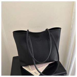 Close-up of the embossed leather texture and central logo detail on a black tote bag