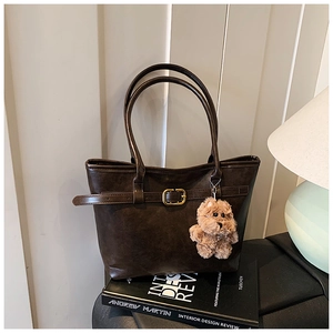 Detail of dark brown tote bag with retro texture, gold buckle and plush bear charm
