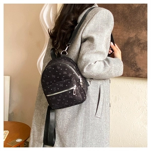 Dettaglio di un mini zaino nero con motivi a cuore su una modella con cappotto