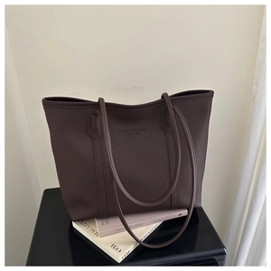 Close-up of dark brown tote bag showing textured lychee leather and embossed lettering