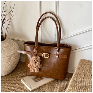 Detail of vintage brown leather tote bag with gold buckle and plush puppy charm
