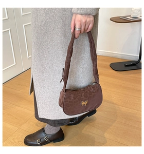 Détail d'un sac d'épaule léopard avec emblème papillon doré et bandoulière plissée
