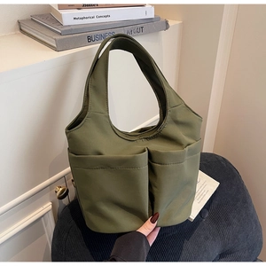 Detail of olive green canvas tote bag showing dual front pockets on a textured chair