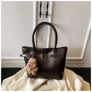 Detail of dark coffee tote bag with decorative buckle and plush dog charm on white blazer