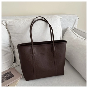 Detail of dark brown leather tote bag with fashion text on a minimalist sofa