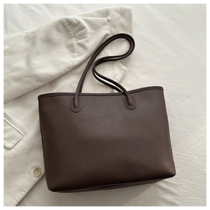 Detail of dark brown lychee texture leather tote bag with long handles on white fabric