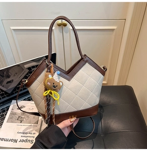 Détail d'un sac cabas beige matelassé avec garniture en cuir marron et pendentif ours
