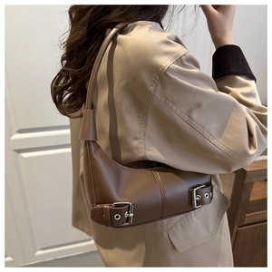 Detail of brown crescent bag showing metal buckles and eyelets in a casual street style