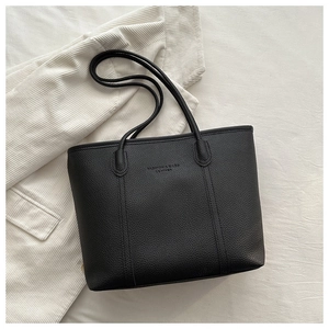 Close-up of minimalist black tote bag with lychee texture and embossed leather logo
