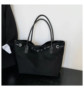 Close-up of black suede tote bag featuring decorative belt with silver metal eyelets