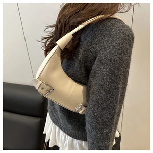 Detail of a creamy white crescent underarm bag with silver metal buckle on a model