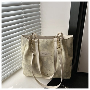 Detail of star and moon printed beige tote bag with gold chain strap on window sill