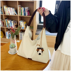 Detail of off-white canvas tote bag with brown shoulder strap and plush dog charm