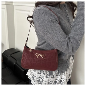 Detail view of burgundy shoulder bag with leopard texture and golden bow hardware