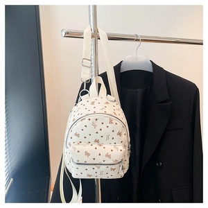 Dettaglio mini zaino in velluto beige con fiocchi a cuore appeso a un blazer nero