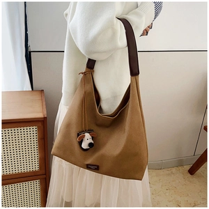 Detail of a large brown canvas hobo bag featuring wide leather strap and cute dog charm
