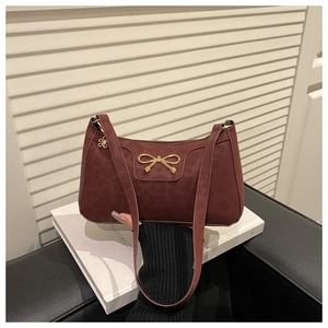 Macro detail of wine red leather underarm bag with gold bow and floral zipper charm