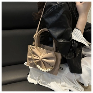 Détail du sac beige avec grand nœud et chaîne en perles porté par un mannequin