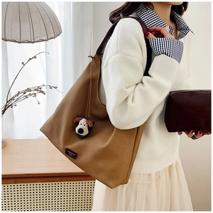 Detail of a large brown canvas tote bag with leather straps and a cartoon dog pendant