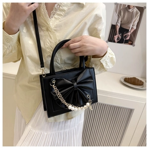 Détail du sac bandoulière noir avec un grand nœud en cuir et une chaîne de perles décorative