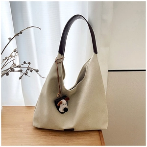 Detail view of beige canvas tote bag with brown leather straps and plush dog charm accessory