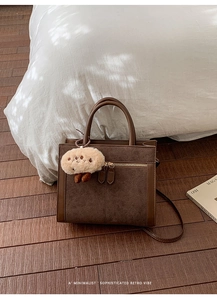 Retro brown suede tote bag with leather trim, featuring round handles and a plush charm